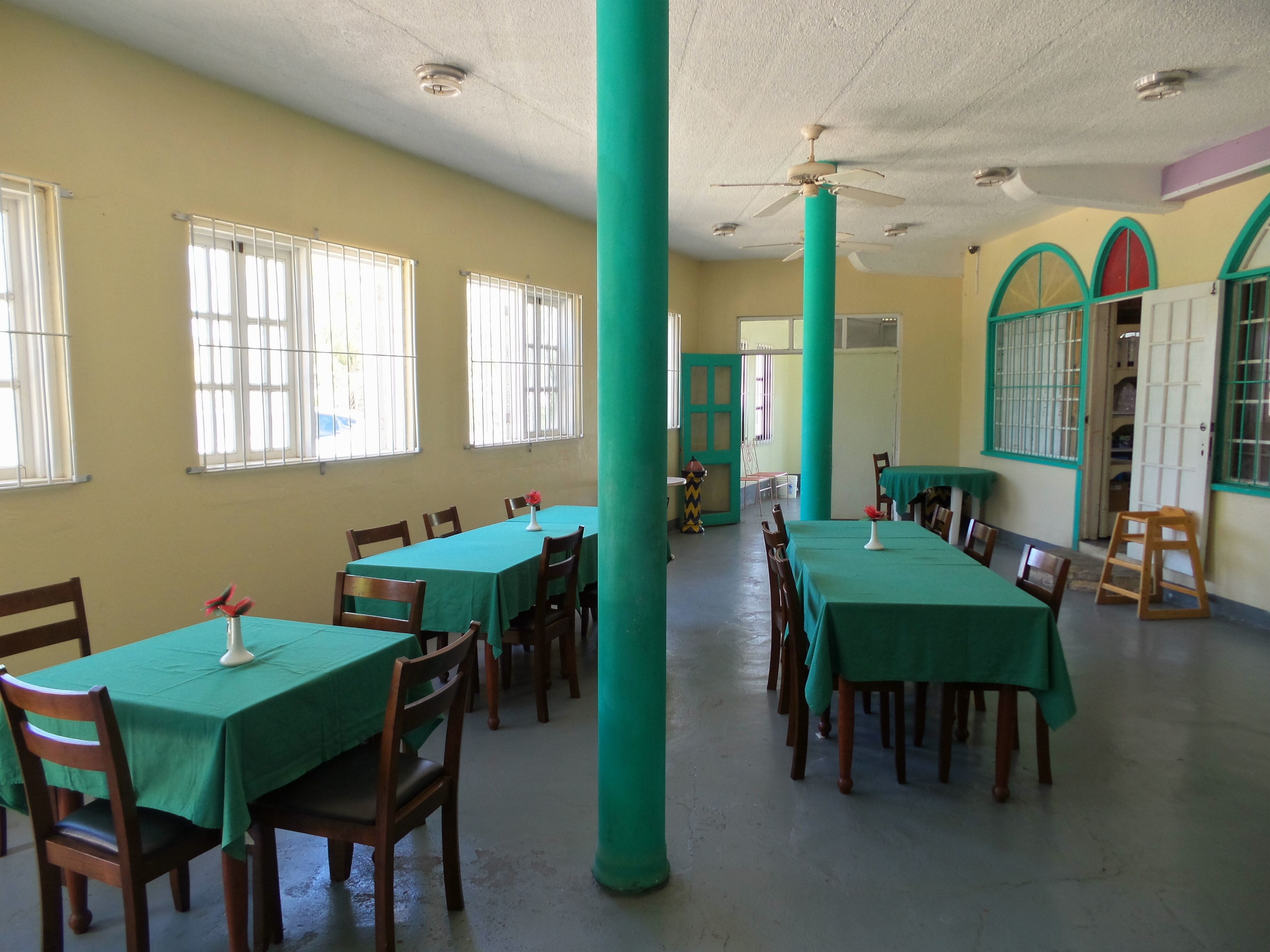 Comedor con mesas y sillas, ventilador de techo y ventanas con rejas.