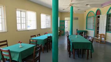 Comedor con mesas y sillas, ventilador de techo y ventanas con rejas.