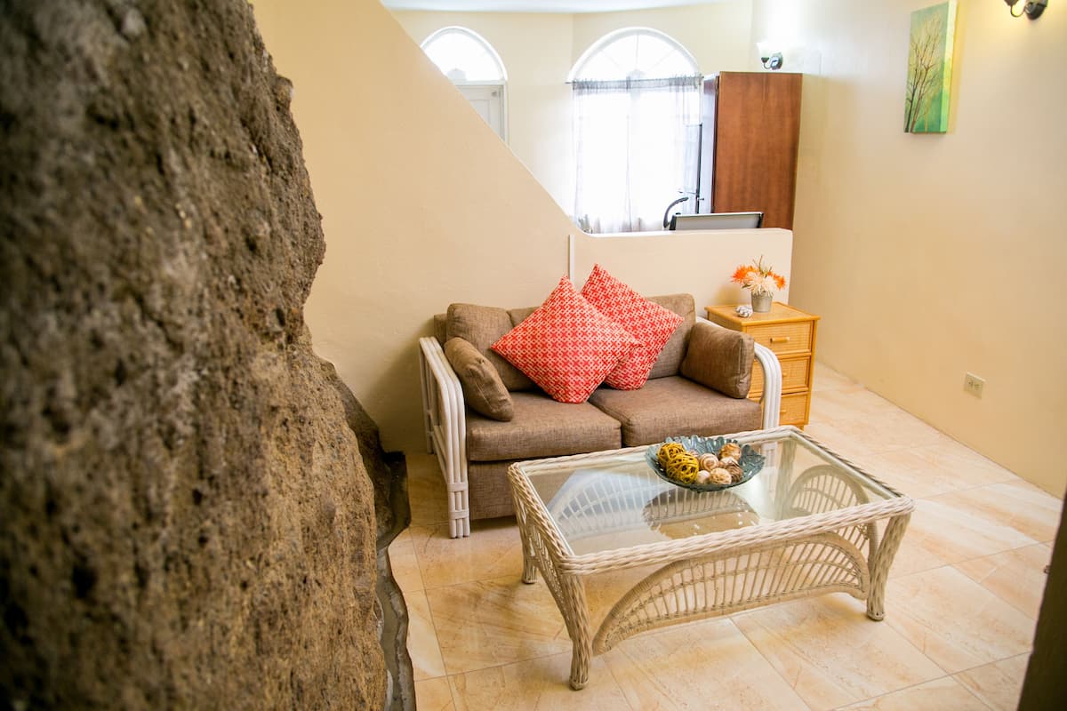 A living room with a sofa, a glass coffee table, and a wooden side table with a vase.