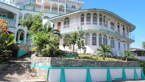 A multi-story building with balconies, a stone retaining wall, and tropical landscaping. - The Apartments at Jolly Castle (Jolly Harbour)