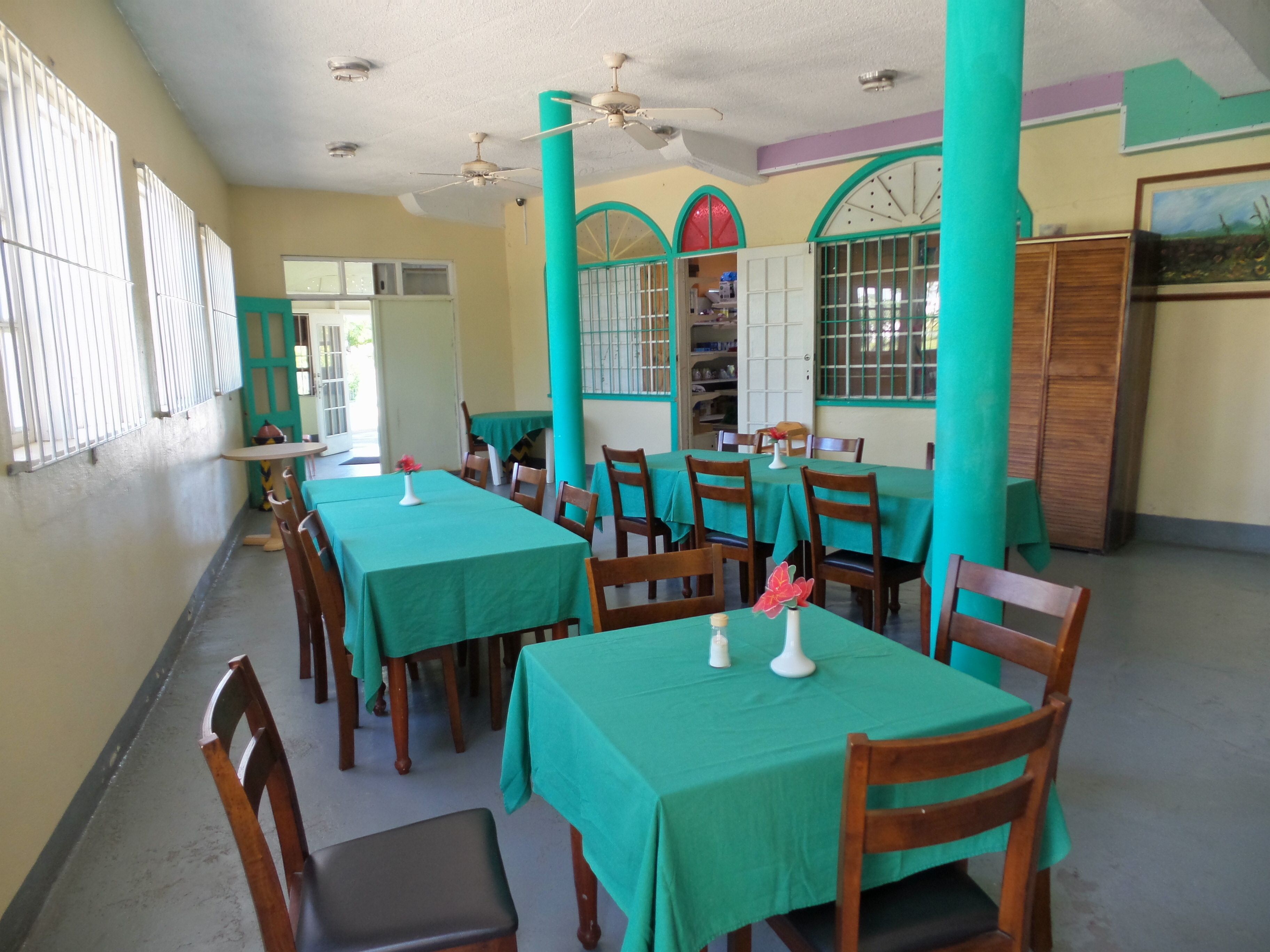 Un comedor con mesas cubiertas de manteles verdes, sillas de madera y ventiladores de techo.