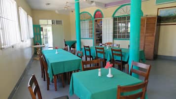 Un comedor con mesas cubiertas de manteles verdes, sillas de madera y ventiladores de techo.