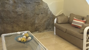 A cozy living room with a stone wall, a glass-top table with decorative items, and a brown sofa with striped pillows. - The Apartments at Jolly Castle (Jolly Harbour)