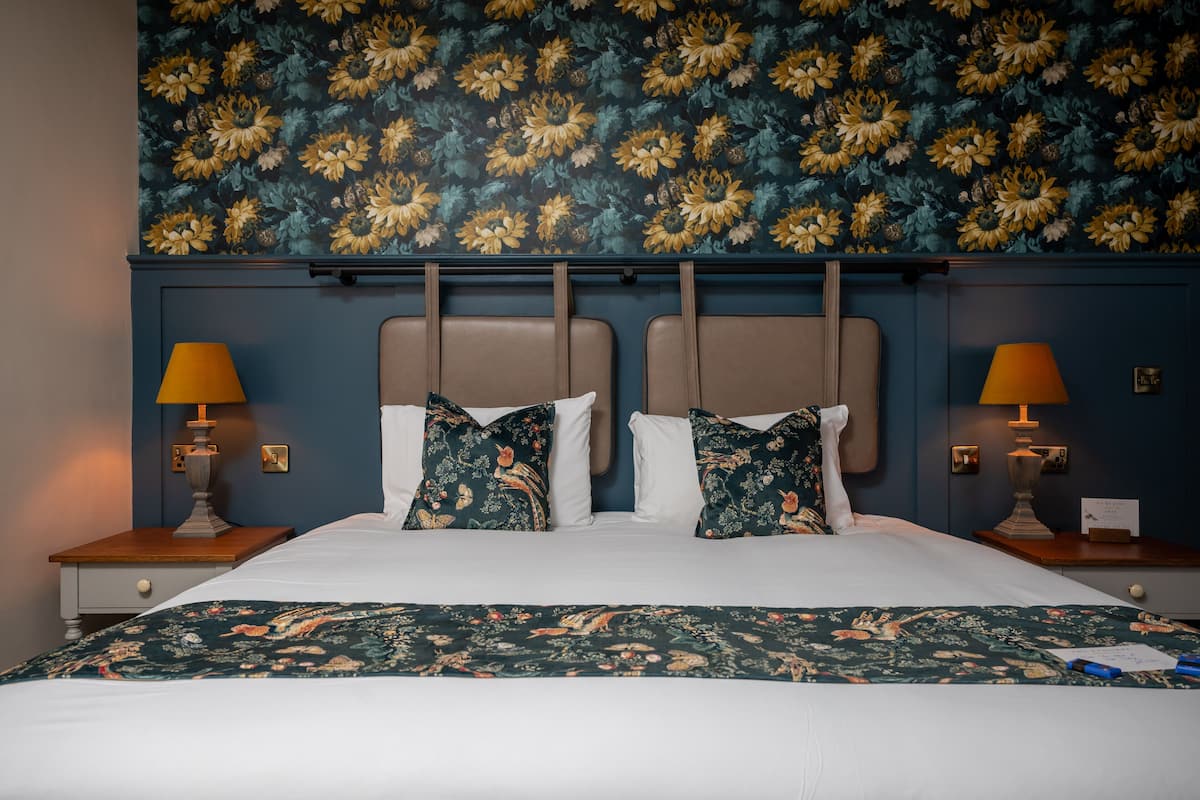 Un letto con cuscini a motivi floreali, una coperta coordinata e una parete rivestita con carta da parati a fiori.