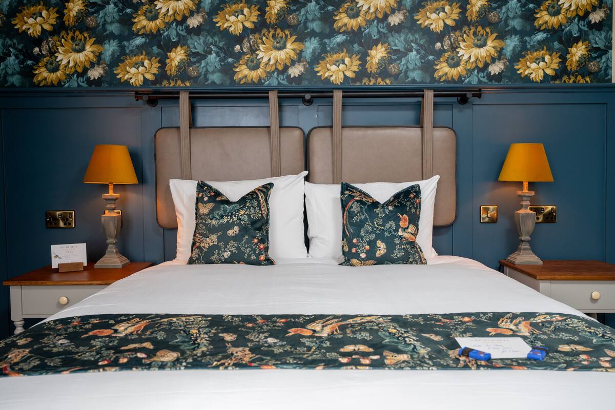 Un letto rifatto con lenzuola a motivi floreali, due abat-jour e una parete decorata con un motivo floreale.