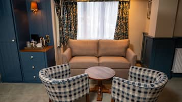 Una habitación con sofá, dos sillones a cuadros, una mesita, una lámpara, una ventana con cortinas, un armario y un radiador.