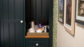 A dark wooden cabinet with a drawer containing a tea kettle, a grater, and a small box.