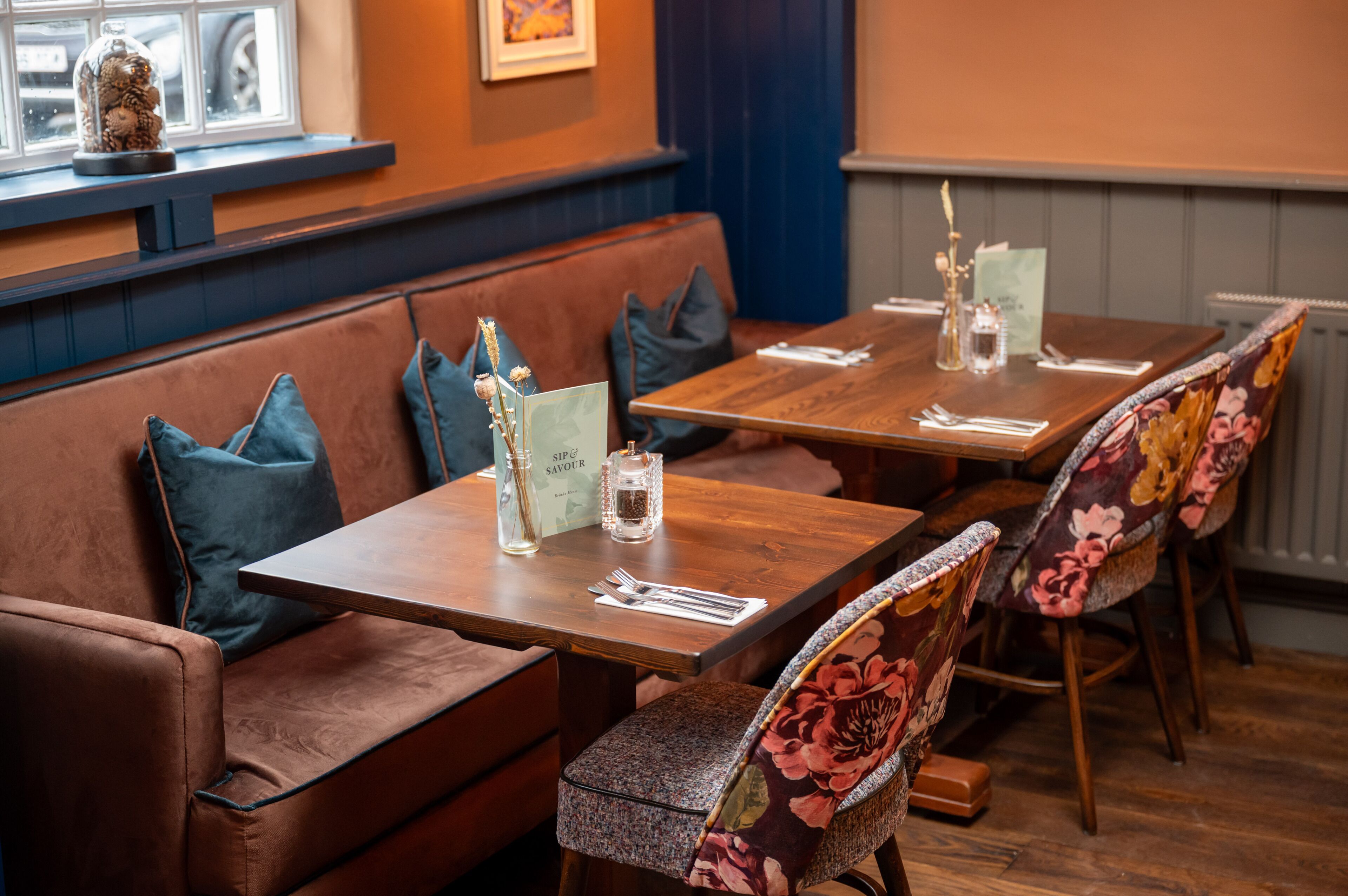 A restaurant with wooden tables and cushioned seating, a window with a decorative item, and a wall-mounted menu.