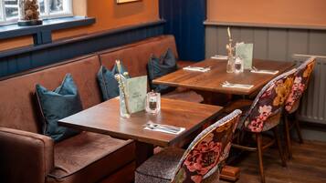 A restaurant with wooden tables and cushioned seating, a window with a decorative item, and a wall-mounted menu.