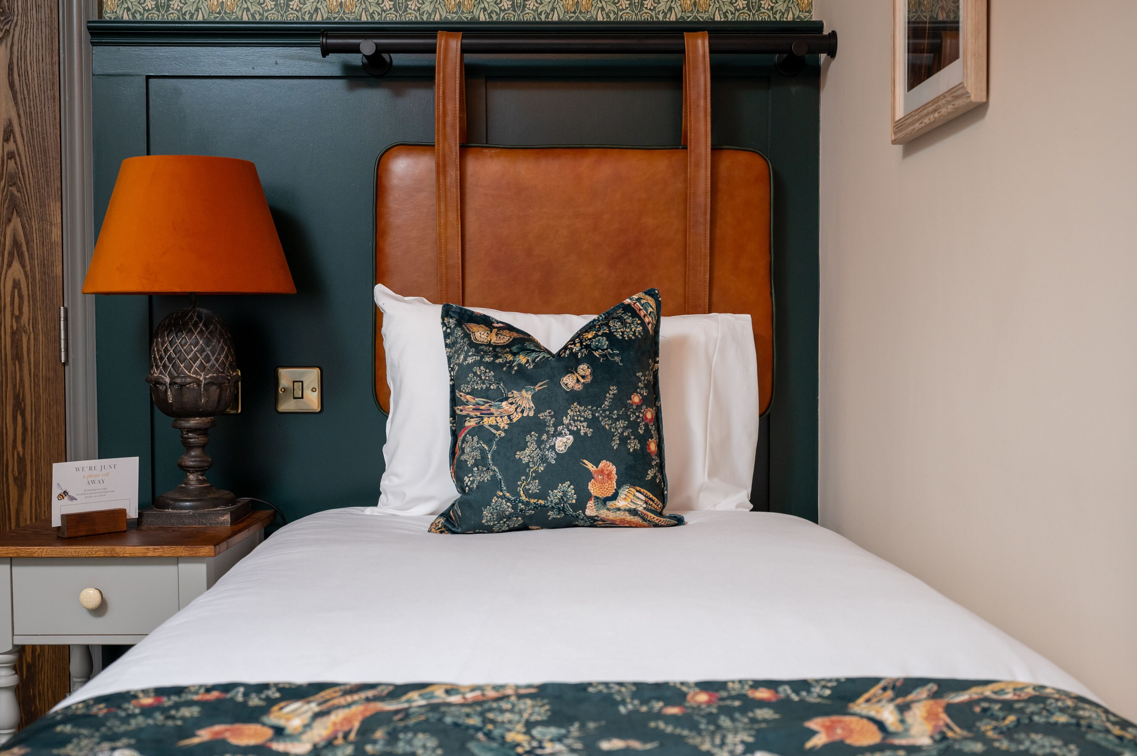 A neatly made bed with a floral-patterned bedspread, a wooden headboard, and a single decorative pillow.