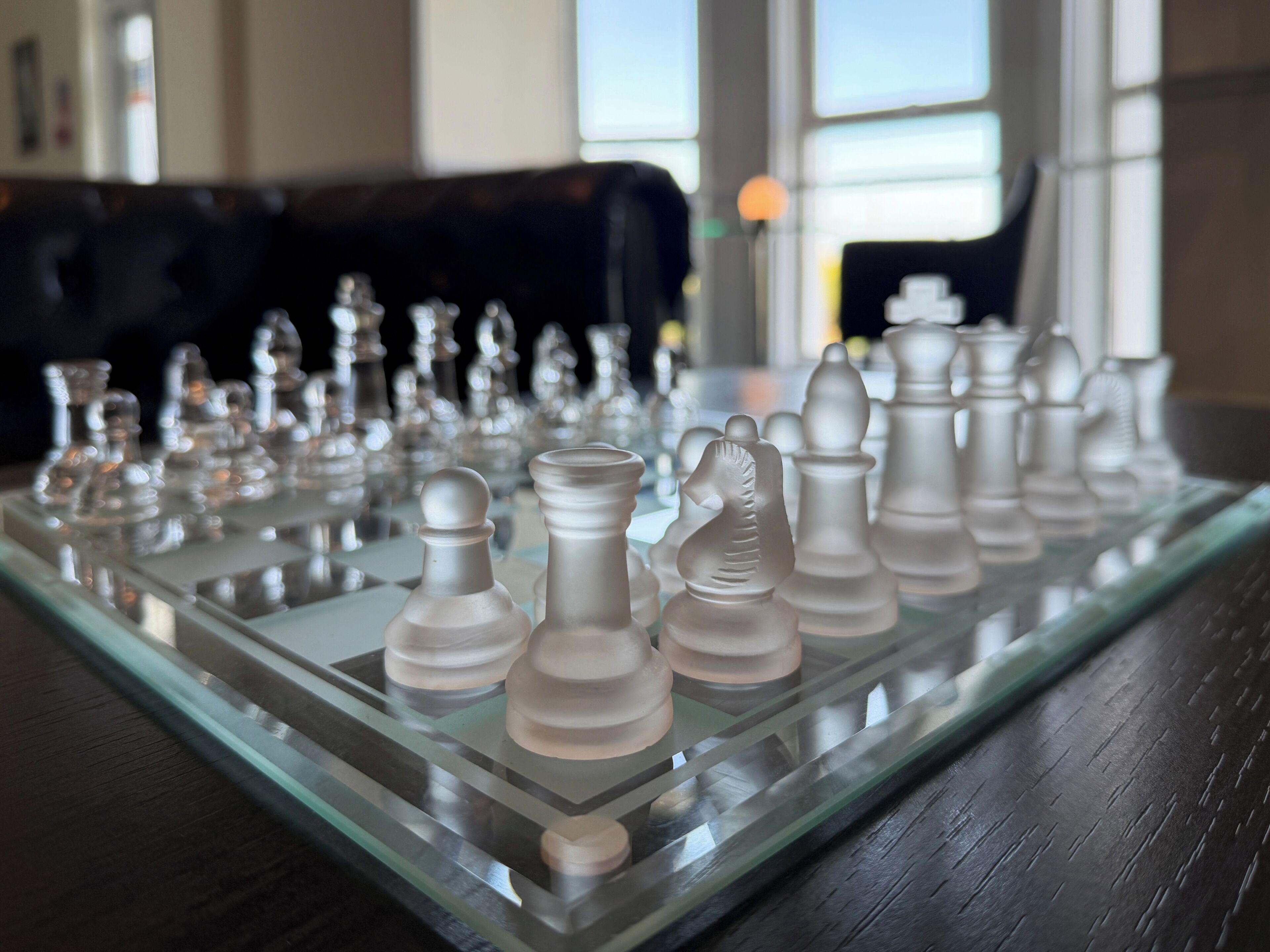 A chessboard with pieces on a glass table.