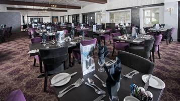 A spacious dining area with multiple tables set for guests, featuring dark tables, purple chairs, and a carpeted floor.