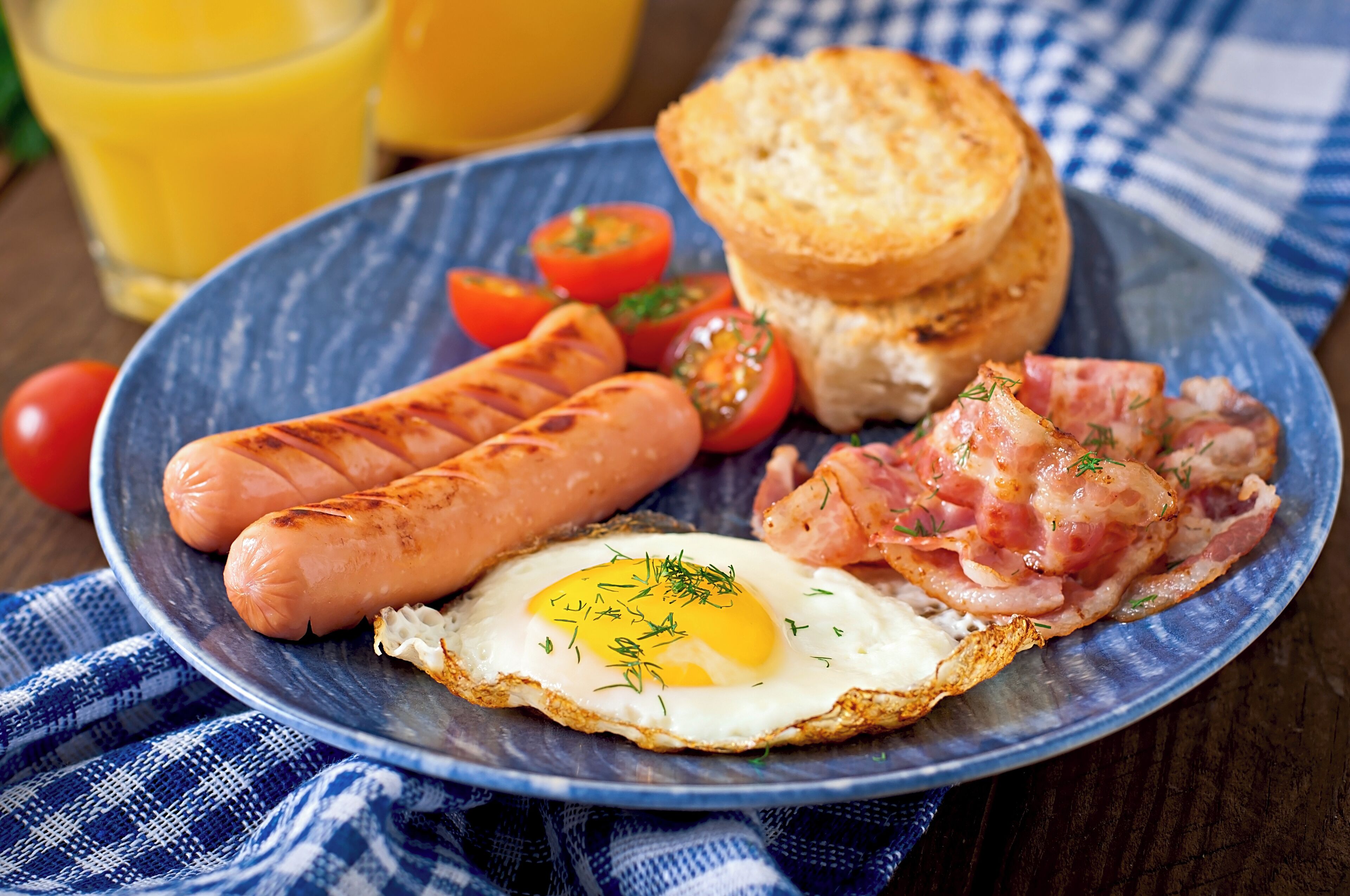 A plate with grilled sausages, a fried egg, bacon, toast, and tomatoes.
