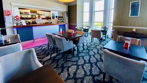 A restaurant with a bar area, multiple tables and chairs, and large windows allowing natural light. - The Esplanade Hotel by Compass Hospitality (Paignton)
