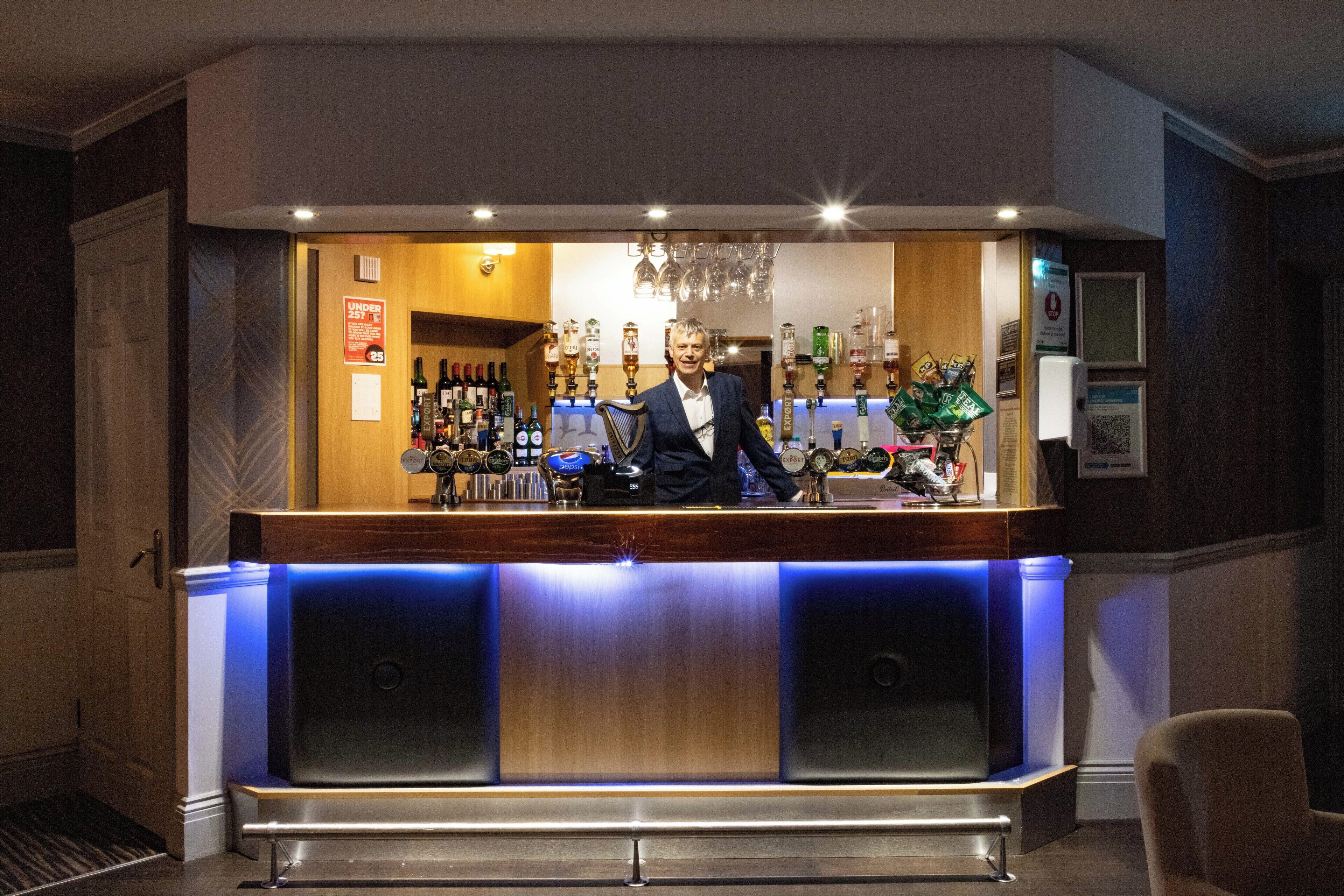 A bar area with a bartender, a wooden counter, and a variety of bottles and glasses.