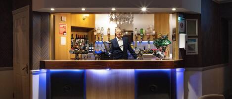 A bar area with a bartender, a wooden counter, and a variety of bottles and glasses.