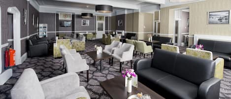 A hotel lobby with a mix of seating options including sofas, chairs, and a coffee table with a tray of coffee and pastries.