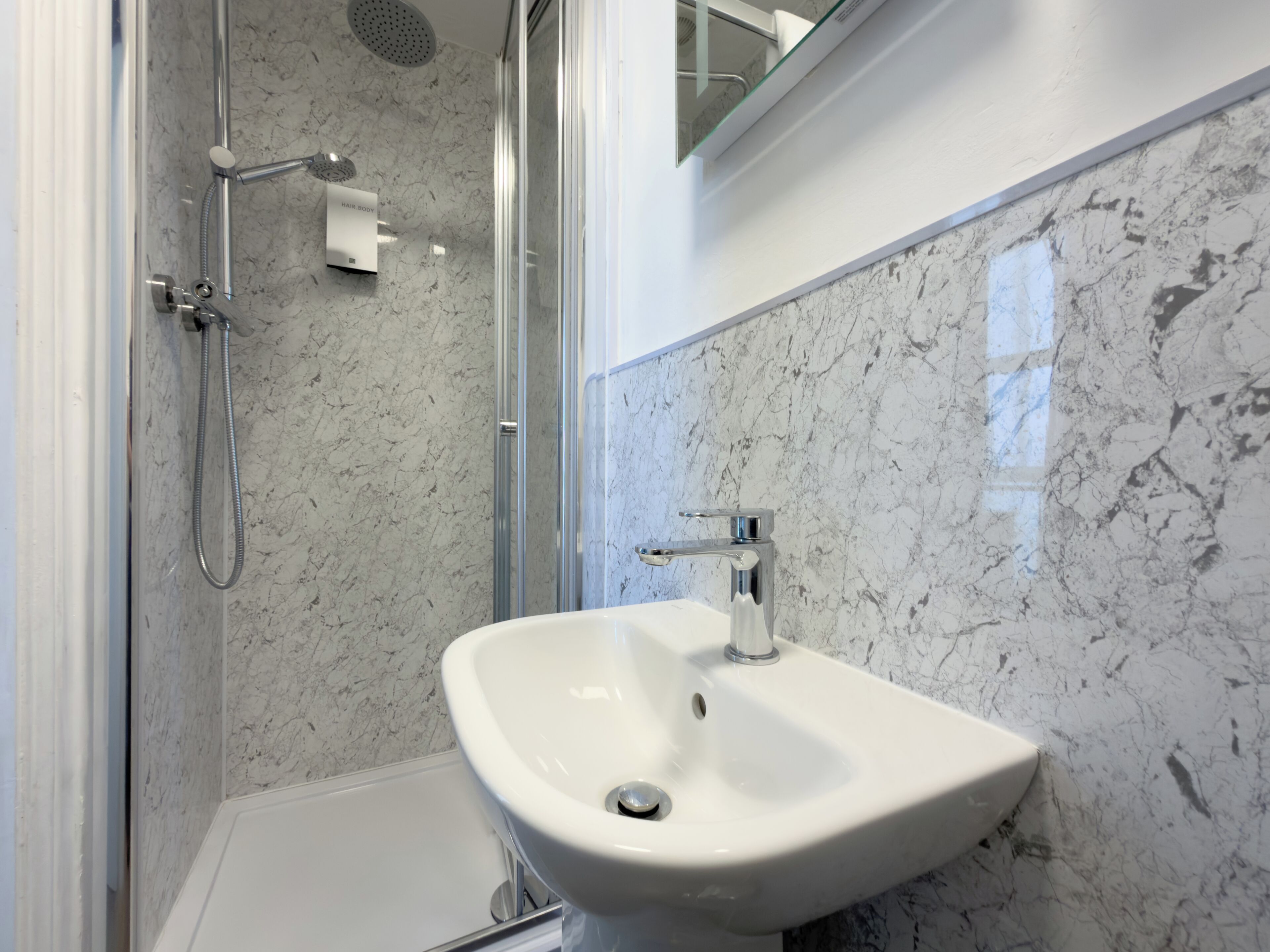 A bathroom with a shower, a sink, and a marble wall.