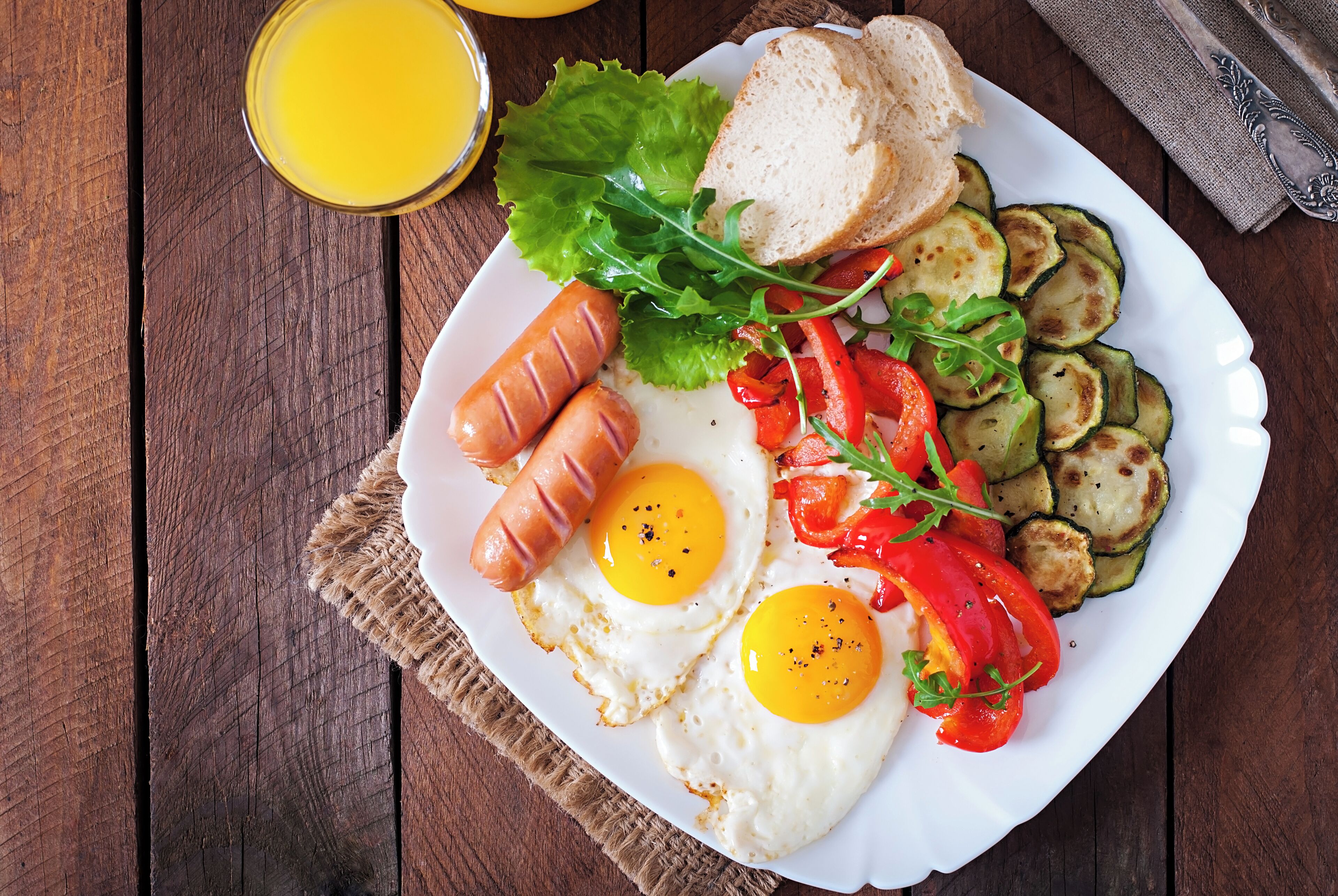Un plato de comida para el desayuno con salchichas, huevos, calabacín y tomates sobre una mesa de madera.