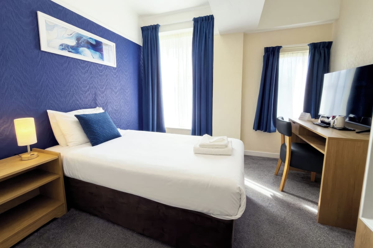 A hotel room with a bed, desk, TV, and a painting on the wall.