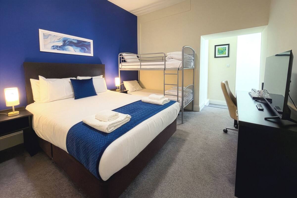 A hotel room with a bunk bed, a desk with a computer, and a painting on the wall.