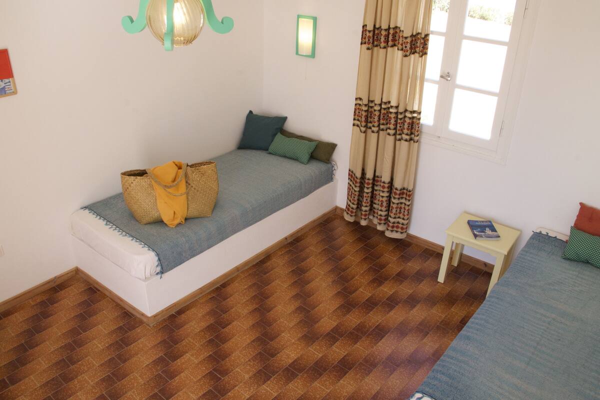 A small, cozy room with a single bed, a small table, and a window with curtains.