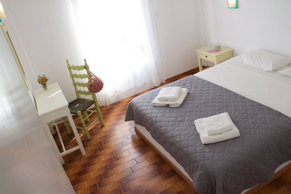 A bedroom with a bed, a chair, a small table, and a nightstand.