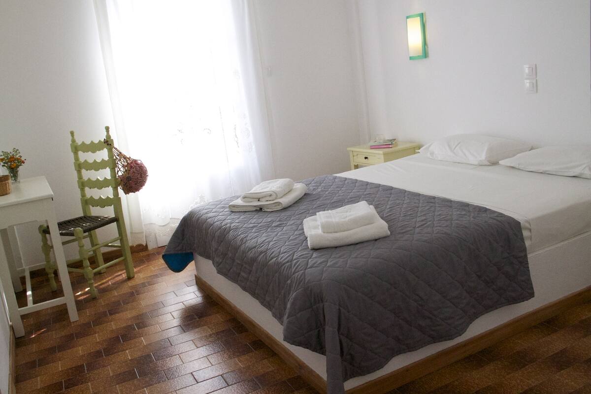 A bedroom with a bed, a chair, a bedside table, and a window with curtains.