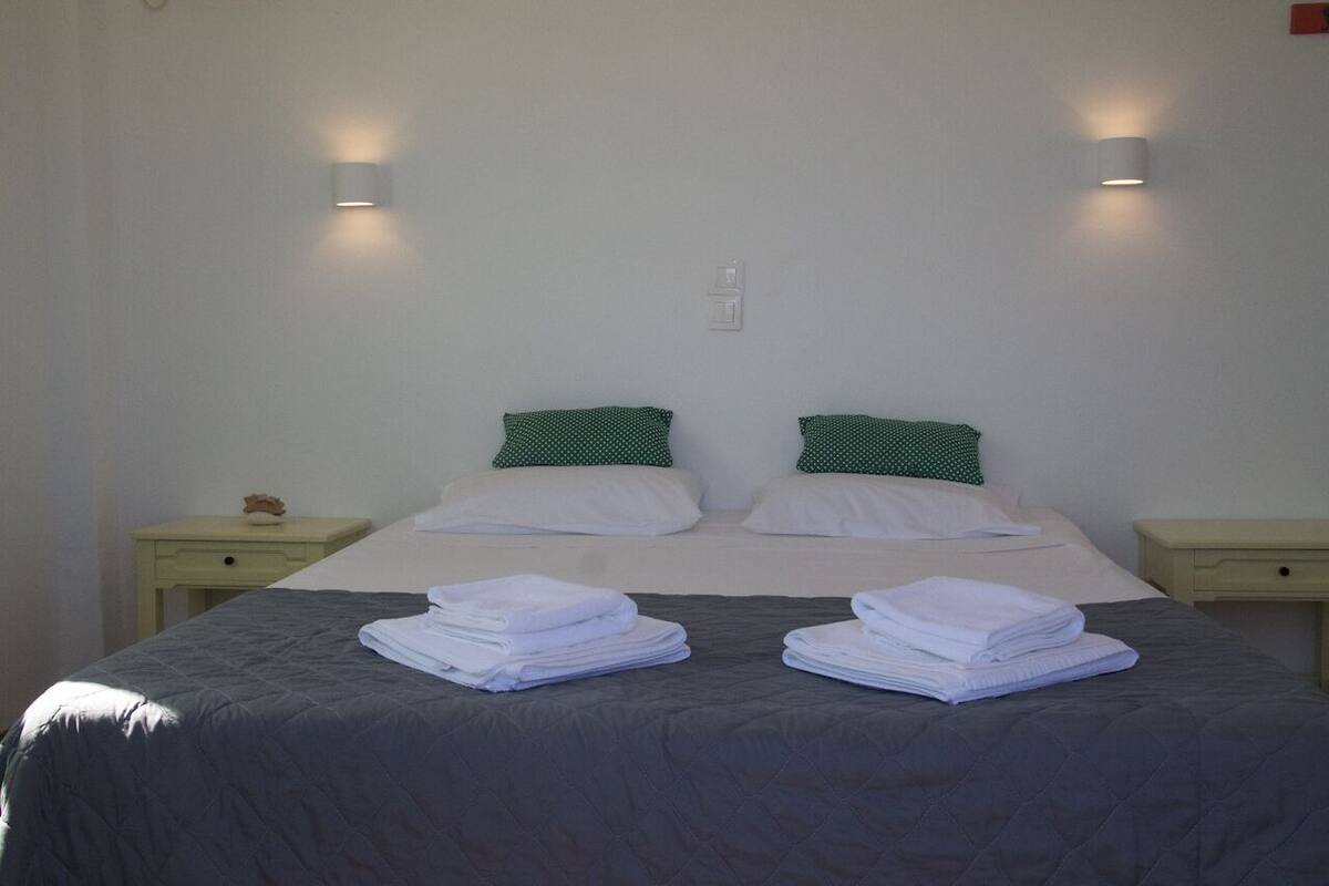 A neatly made bed with two pillows, two bedside tables, and a wall-mounted light fixture.