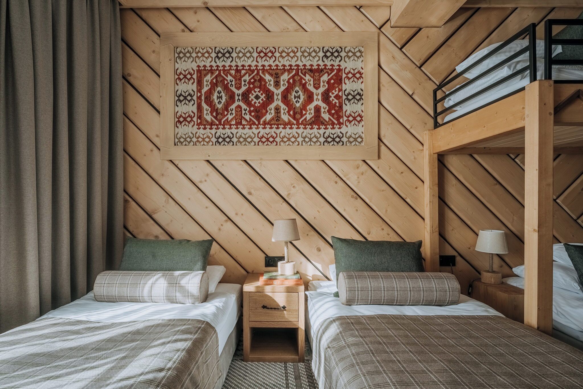 Une pièce chaleureuse avec deux lits, un plafond en bois, un tapis à motifs et une petite table avec une lampe.