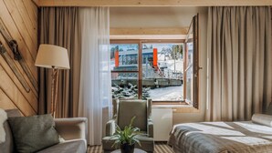 Ein Hotelzimmer mit Bett, Sofa, Sessel, Lampe, Pflanze und Fenster mit Blick auf eine Seilbahn und verschneite Landschaft.
