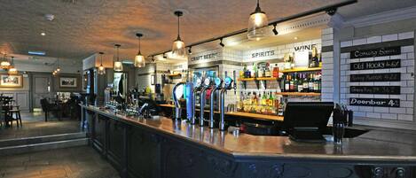 A bar area with a counter, multiple taps, and shelves stocked with bottles.