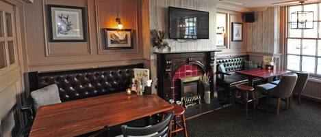 A cozy pub with a wooden bar, a fireplace, and comfortable seating.