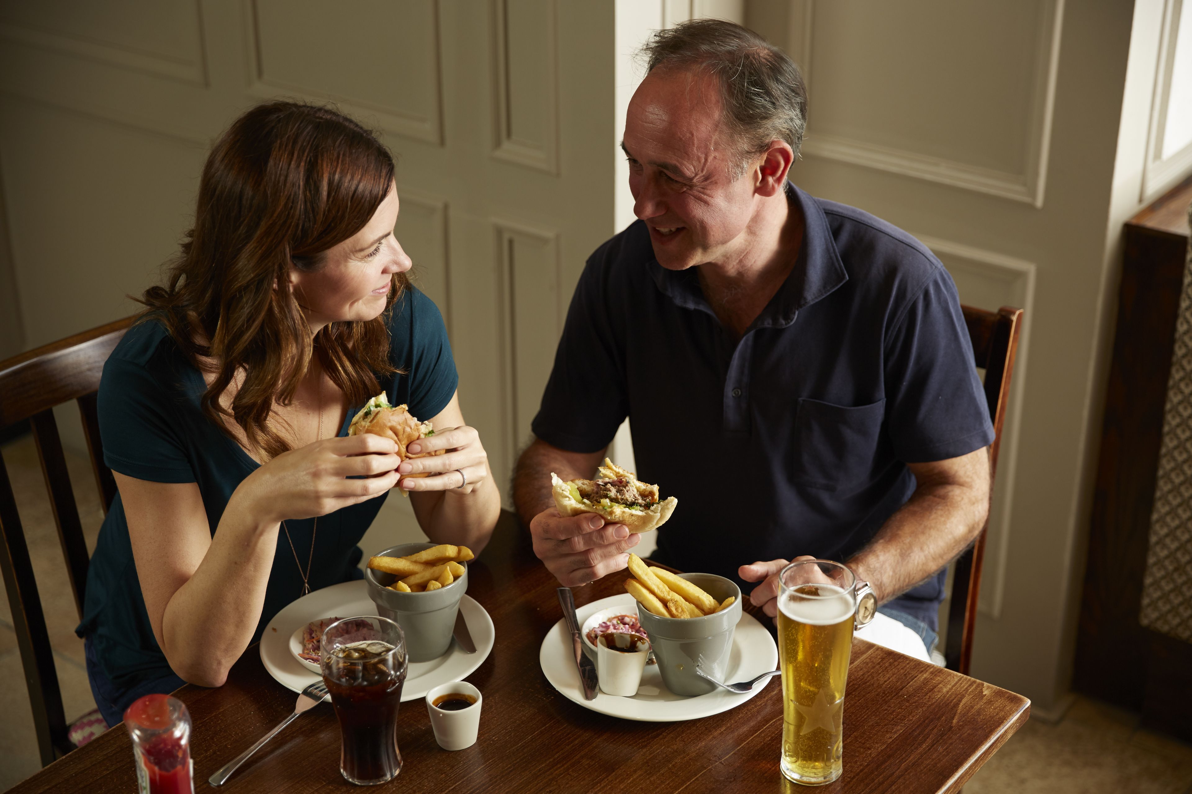 A dining table with a meal consisting of burgers, fries, and a beer.