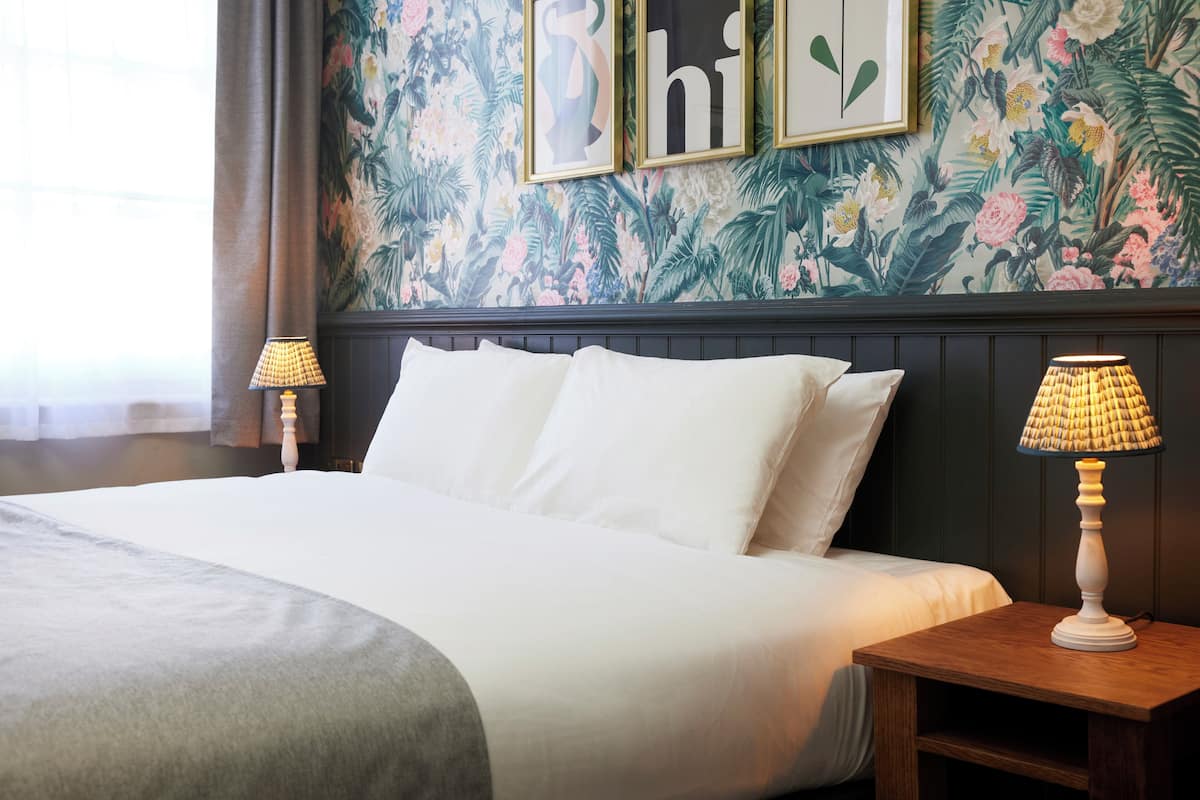 Une chambre d’hôtel avec un grand lit, deux lampes de chevet et un papier peint à motifs floraux.