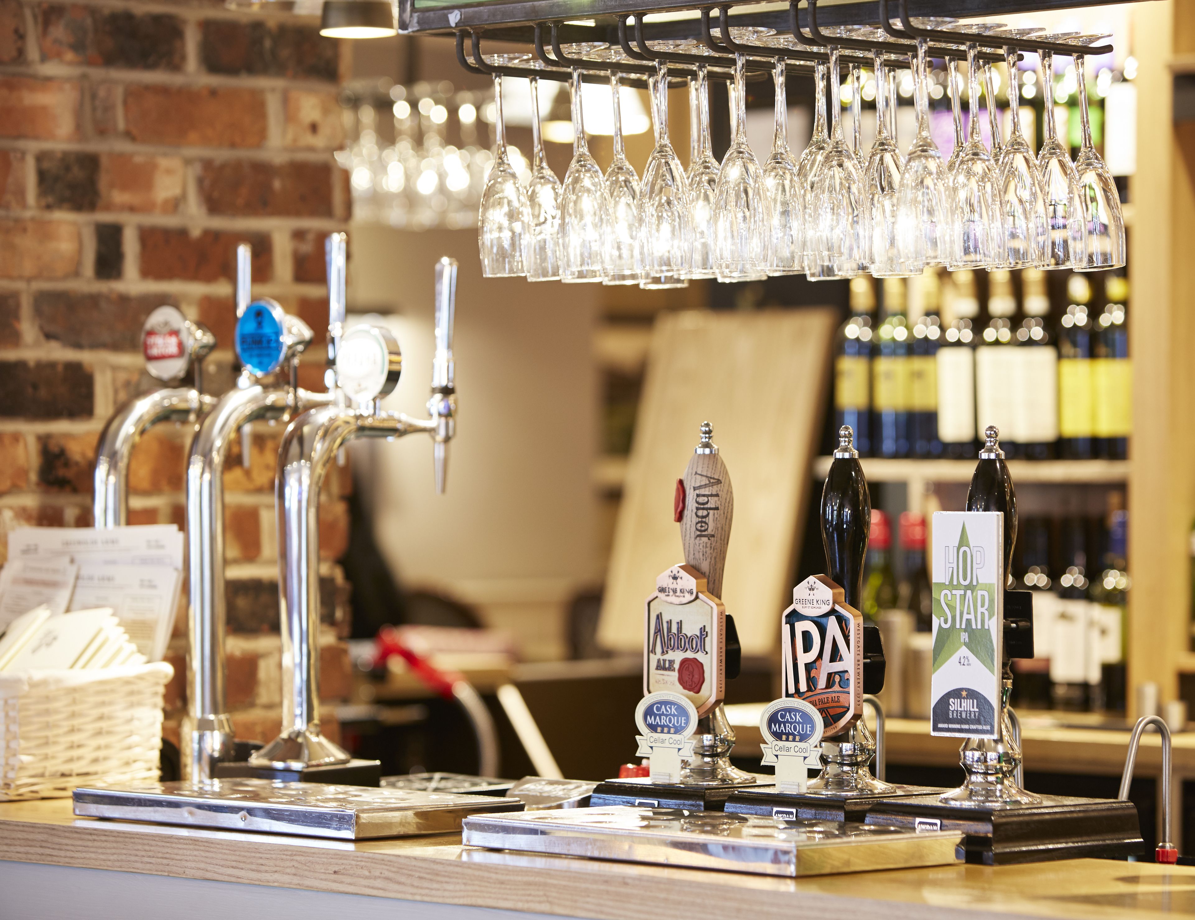 A bar area with multiple taps, a selection of beer bottles, and a glass rack.