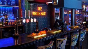 A bar area with a neon sign reading "The White Hart," a beer tap, and a cash register. - The White Hart Hotel by Greene King Inns (Buckingham)