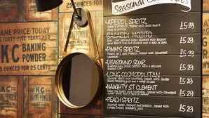 A menu board listing seasonal cocktails with prices, a hanging lamp, and vintage baking powder advertisements on the wall. - The White Hart Hotel by Greene King Inns (Buckingham)