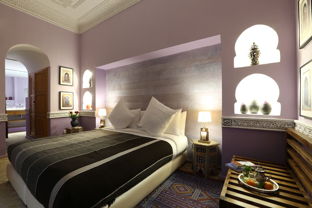 A bedroom with a bed, bedside tables, a bench, and a window with decorative elements.