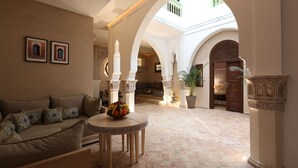 Een ruime zithoek met een bank, een ronde tafel met fruit, en uitzicht op een binnenplaats met bogen en een balkon.