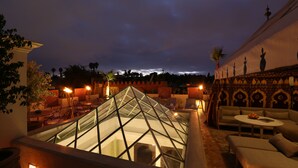 Een terras op het dak met een glazen piramideconstructie, zithoeken en een uitzicht op de skyline van de stad in de schemering.