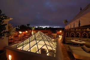 Una terraza en la azotea con una estructura piramidal de vidrio, zonas de estar y vistas al horizonte de la ciudad al atardecer.