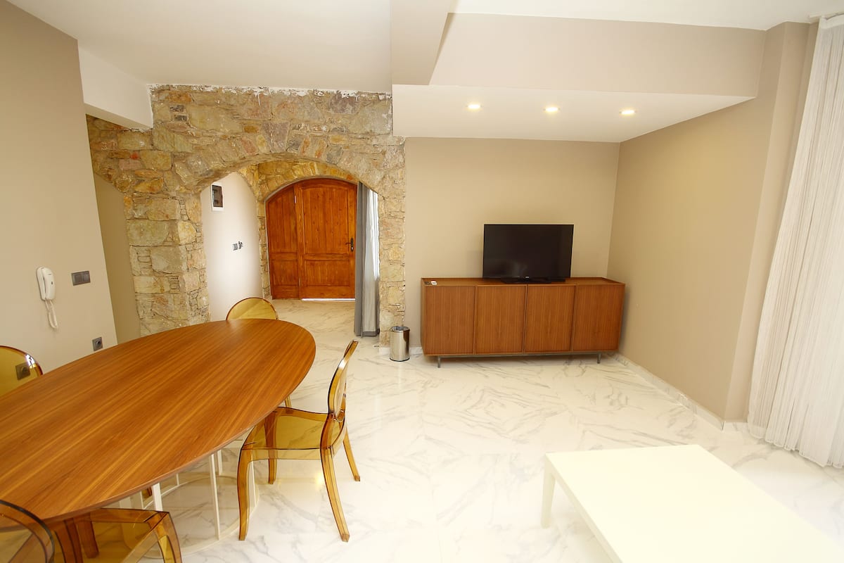 A spacious room with a large wooden dining table, chairs, a stone archway, a wooden cabinet, and a television.