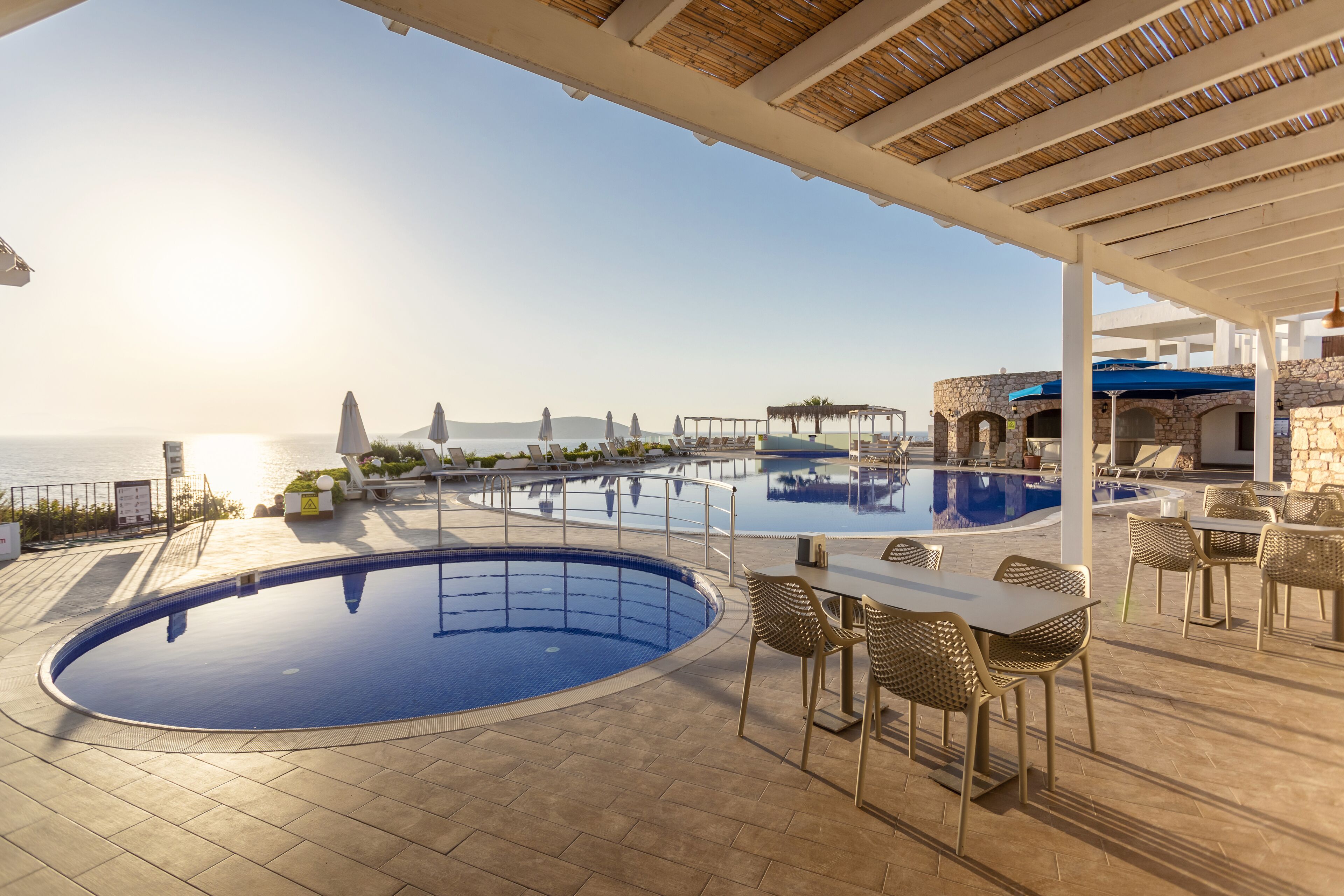 A pool area with a view of the sea, outdoor seating, and a covered patio.