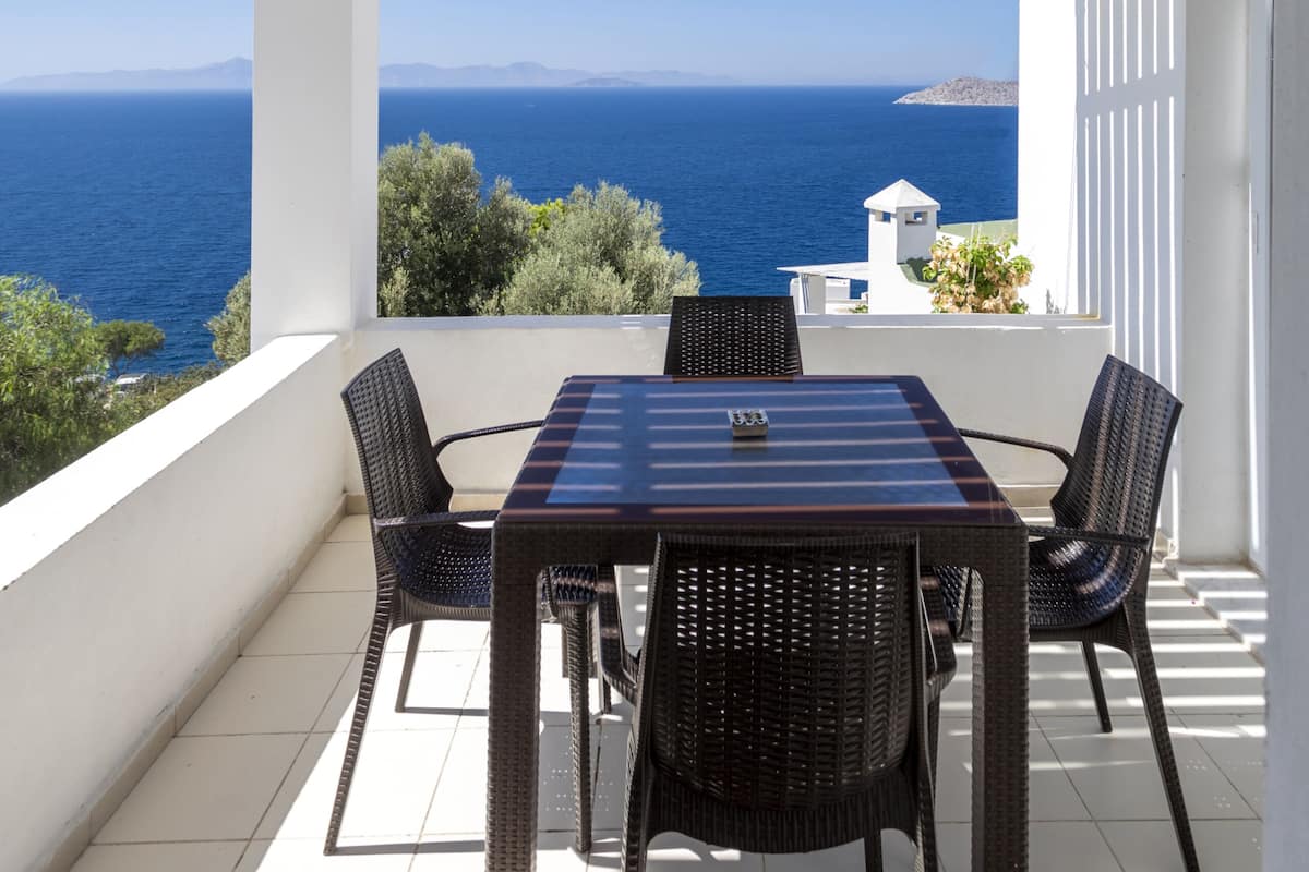A covered outdoor seating area with a table and chairs, overlooking the sea.