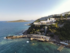 A coastal hotel with multiple buildings, a pier extending into the sea, and a mountainous backdrop. - Vega Aparts (Bodrum)