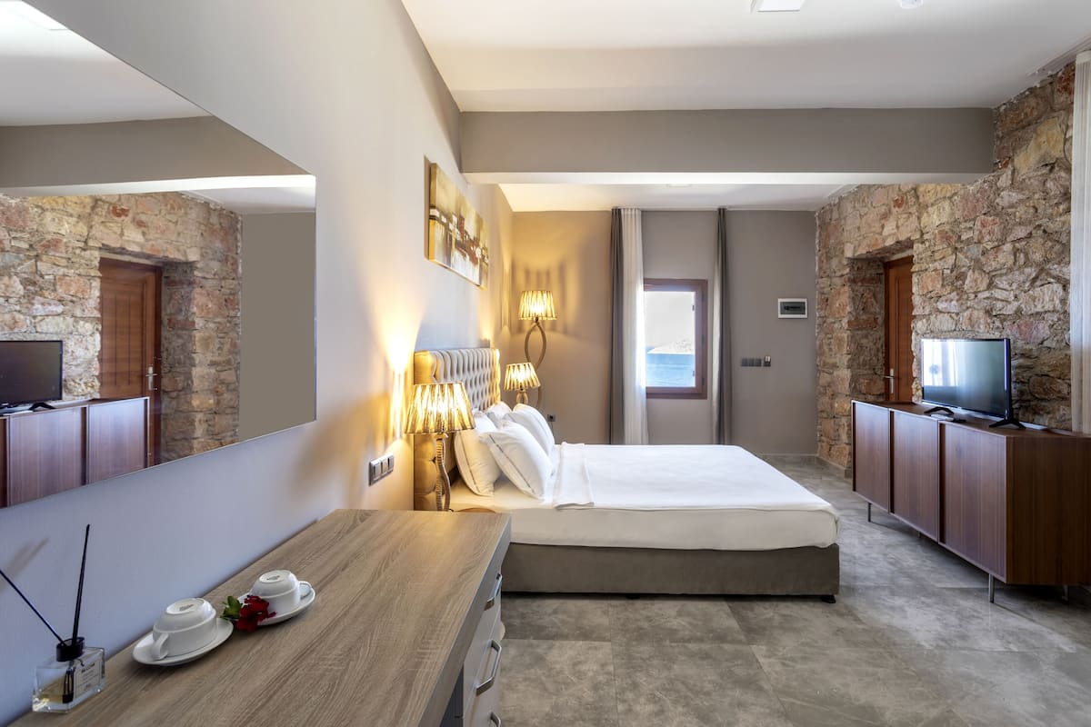 A modern hotel room with a stone accent wall, a large bed, a wooden desk, a television, and a mirror.