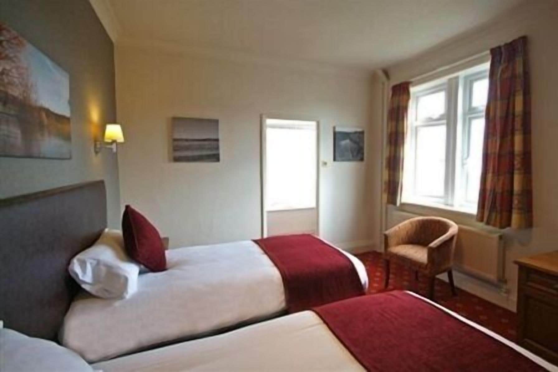 A hotel room with two beds, a chair, a desk, and a window with curtains.