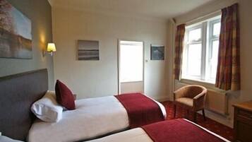 A hotel room with two beds, a chair, a desk, and a window with curtains.