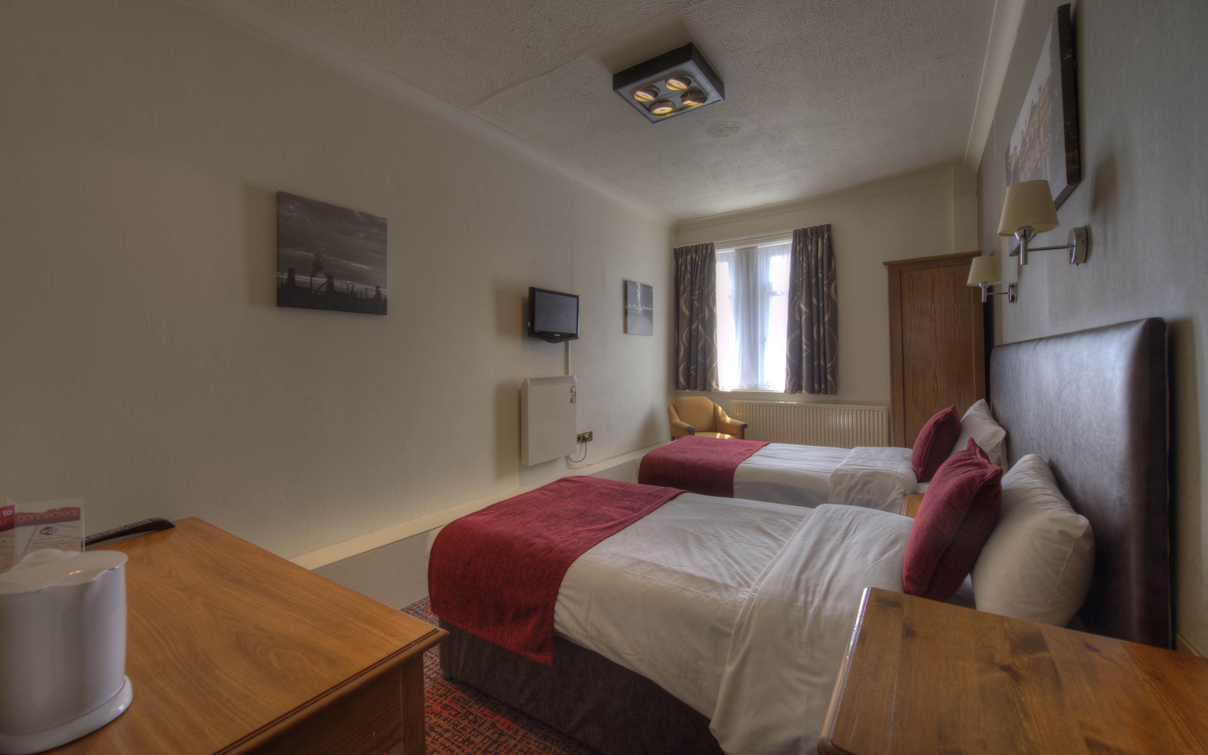 A hotel room with two beds, a desk, a television, and a window with curtains.